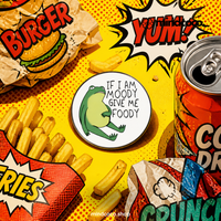 "If Moody Give Foody" enamel pin – lifestyle flat lay, neurodivergent and mental health humour