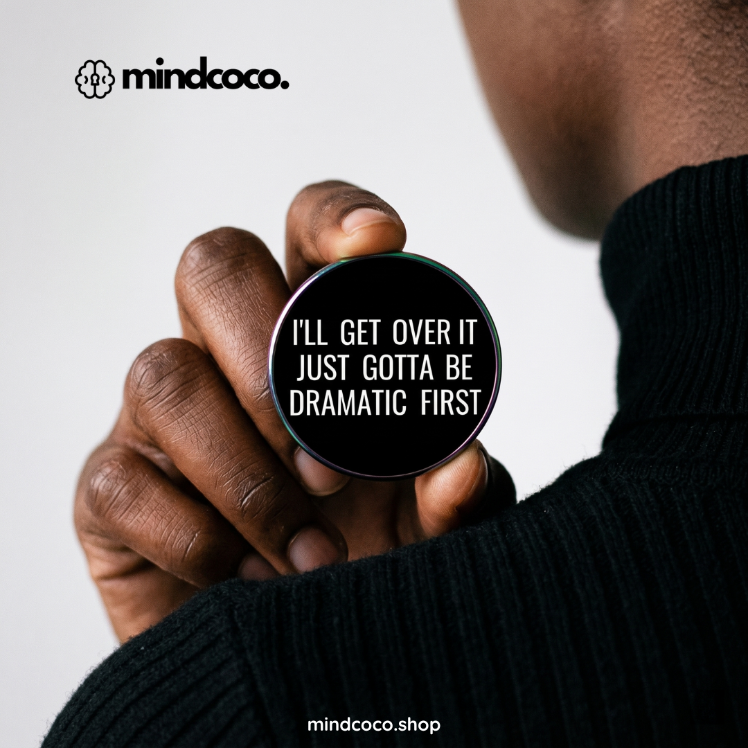 "Gotta Be Dramatic First" enamel pin – lifestyle flat lay, neurodivergent and mental health humour
