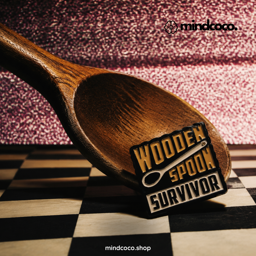 "Wooden Spoon Survivor" enamel pin – lifestyle flat lay, neurodivergent and mental health humour