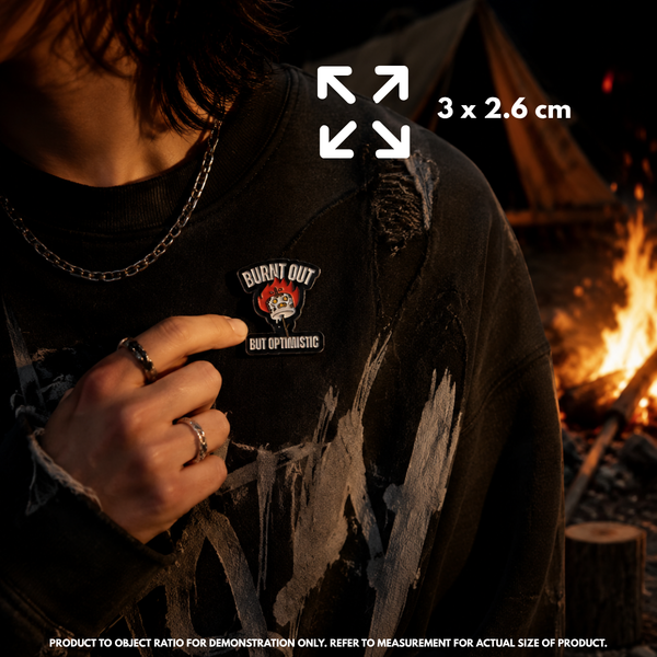 Person holding "Burnt Out But Optimistic" enamel pin showing 3×3cm size