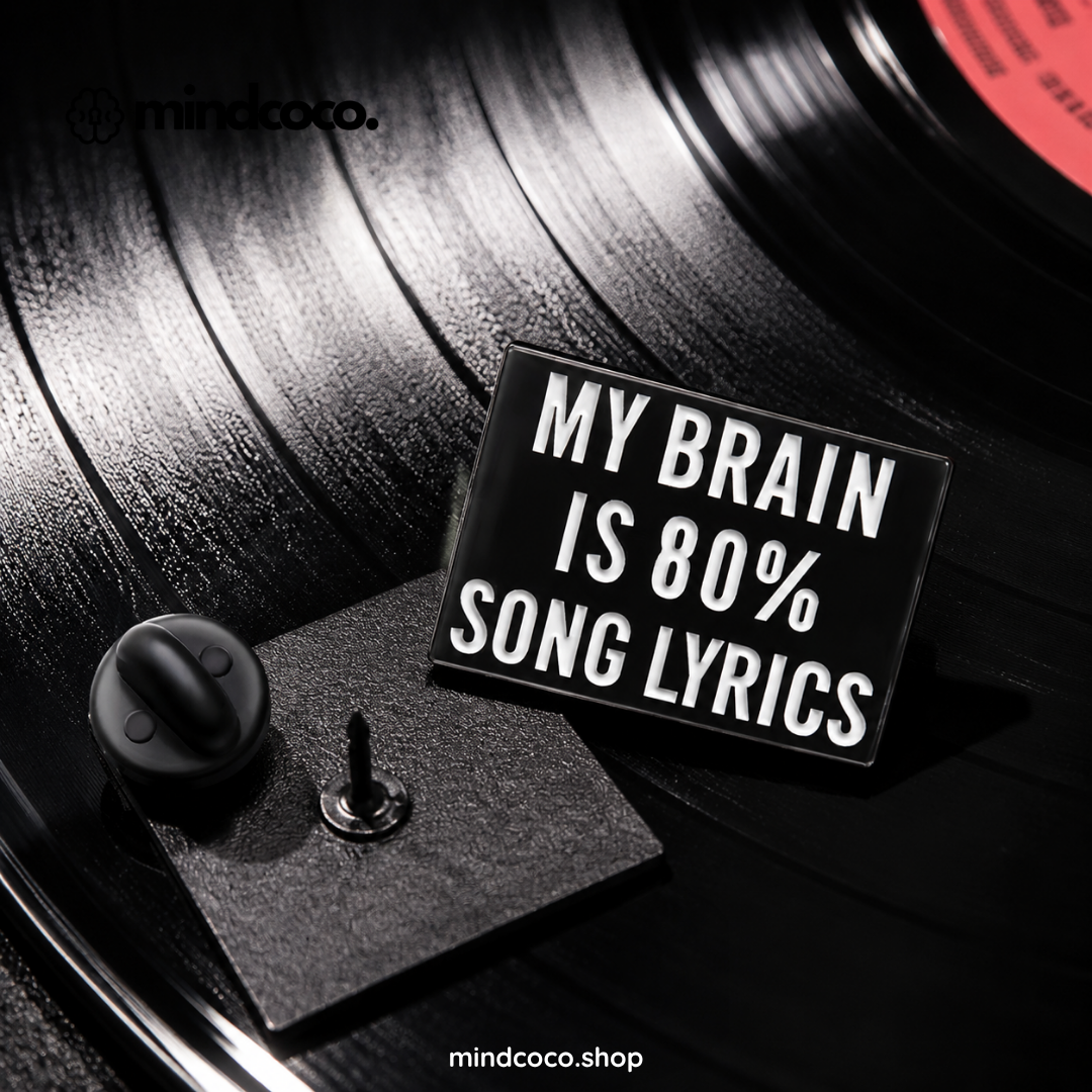 "My Brain is 80% Lyrics" enamel pin – lifestyle flat lay, neurodivergent and mental health humour