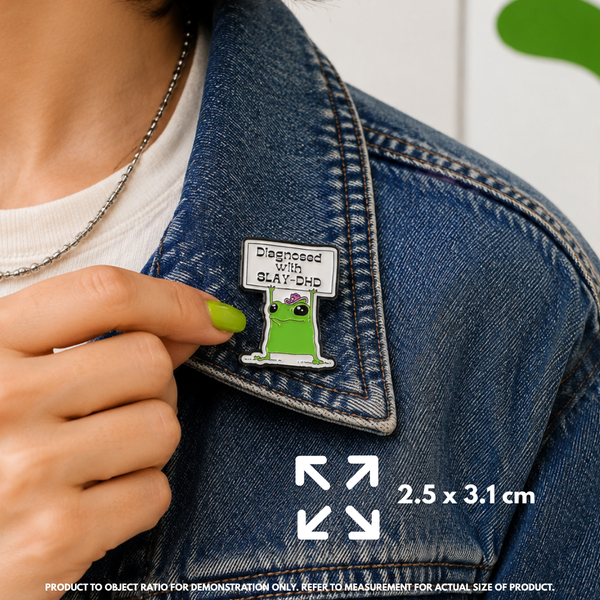 Person holding "SlayDHD" enamel pin showing 3×3cm size