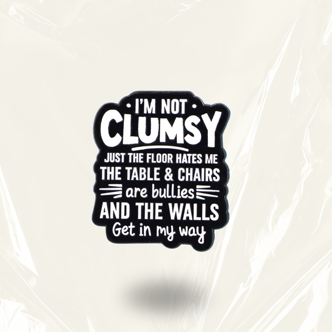 MindCoco "I'm Not Clumsy Just the Floor Hates Me" Pin: A high-contrast black and white text-only enamel badge. This long-form, painfully relatable accessory validates spatial awareness struggles for ADHD and autistic individuals with a touch of defensive humor.