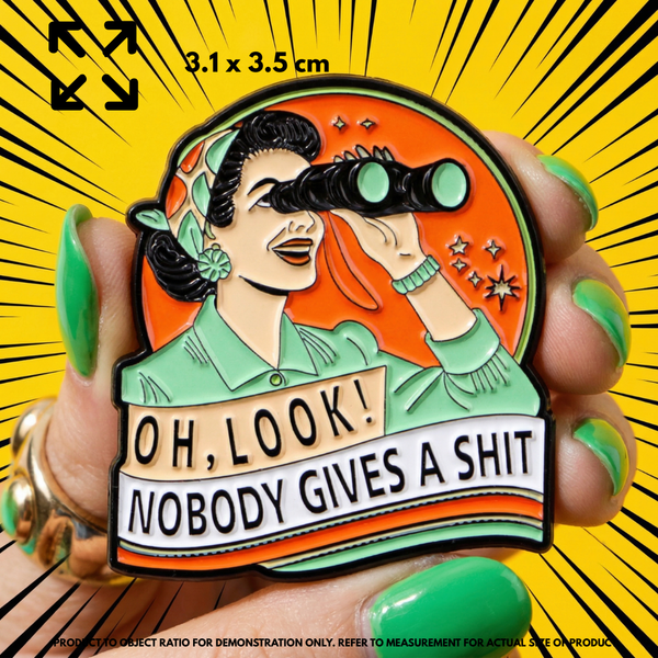 Person holding "OH, LOOK! NOBODY GIVES A SHIT" enamel pin showing 3×3cm size